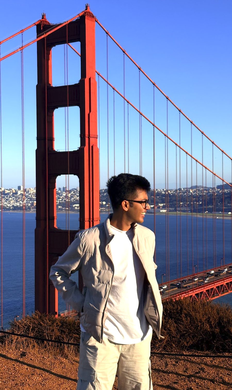Ishaan Godha in a light jacket, smiling, with the Golden Gate Bridge behind him